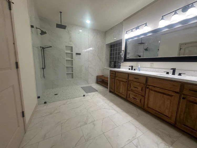 Master bathroom remodel in College Station with white Carrara 24x48 tile, a curbless doorless-entry shower with frameless glass, custom niche, and rainhead with handheld wand